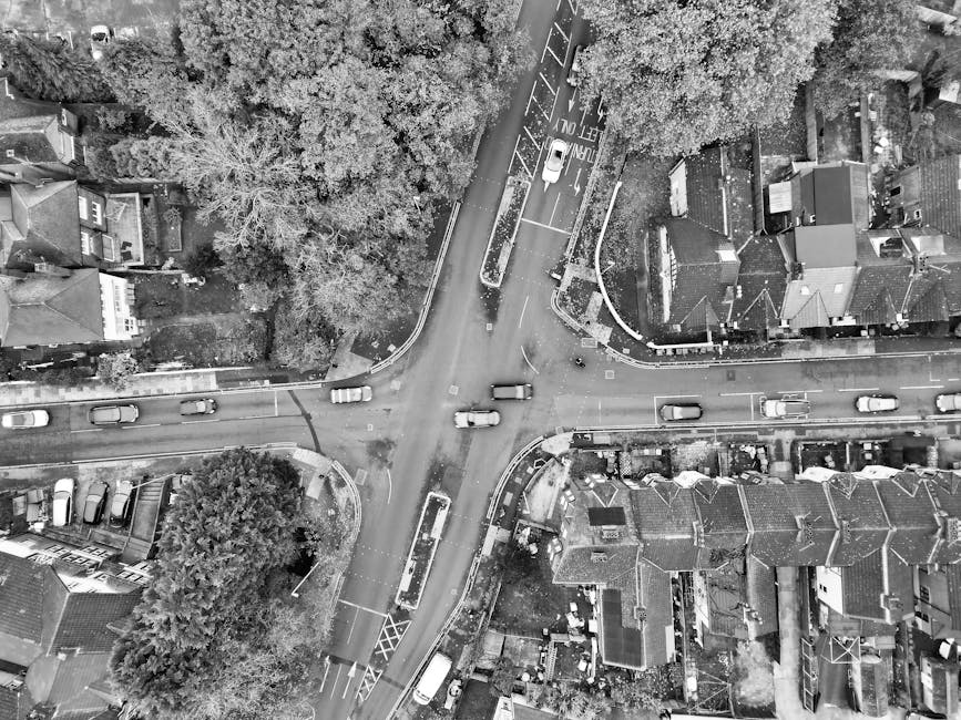 Black and white aerial view of an urban intersection with moving traffic and surrounding buildings.