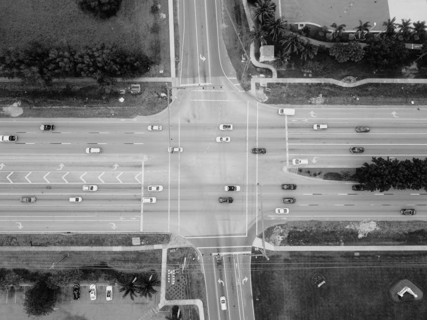 Black and white aerial shot of a busy urban intersection with cars and trees.